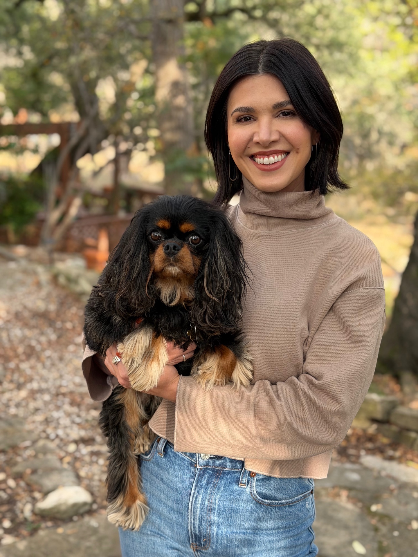 Jean smiling outdoors holding her cavalier spaniel